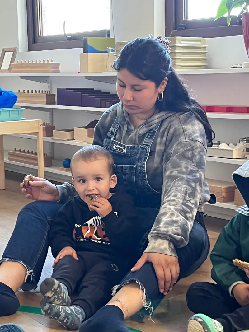 Una adulta acompaña a un niño pequeño junto a los materiales de Aurora.