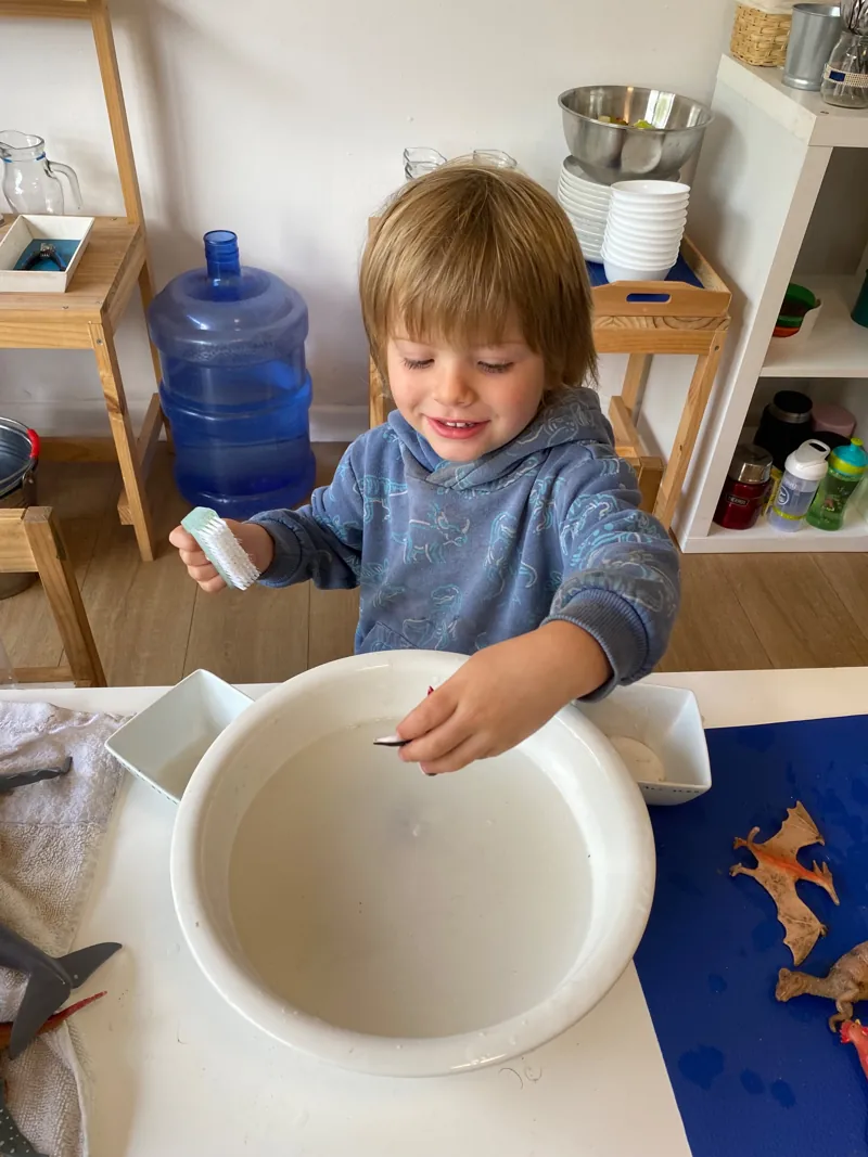 Un niño explora una actividad con agua, un cuenco y una jarra en Aurora.