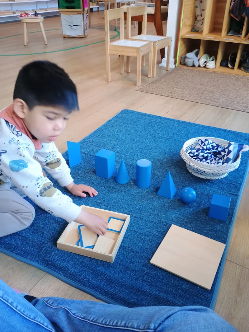 Un niño explora sólidos geométricos sobre una alfombra en Aurora.