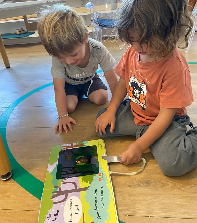 Dos niños miran juntos un libro ilustrado en Aurora.
