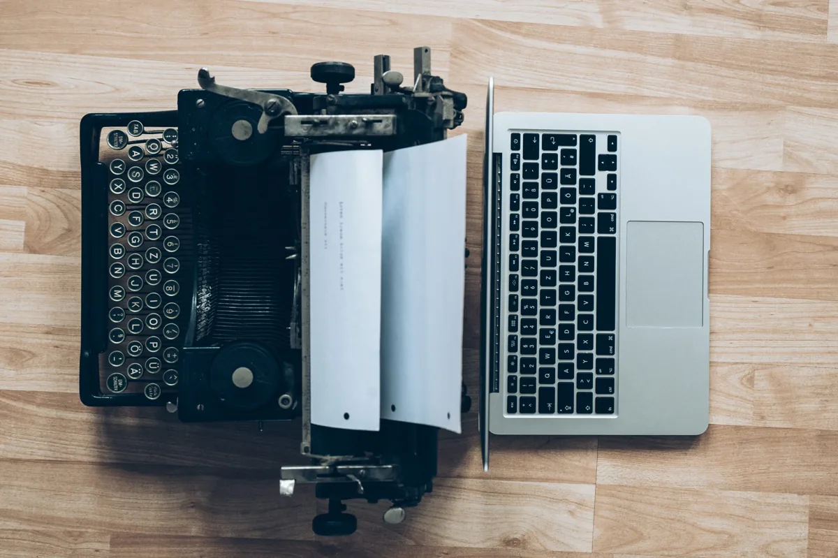 Una máquina de escribir y un computador portátil sobre una mesa de madera.