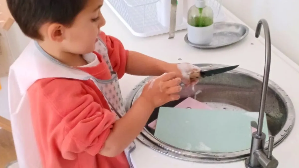 Un niño limpia un cuchillo junto al lavaplatos.